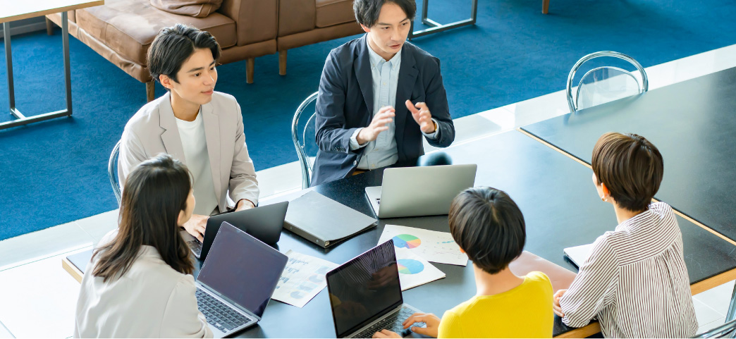 会社のデスクで会議する5人の男女