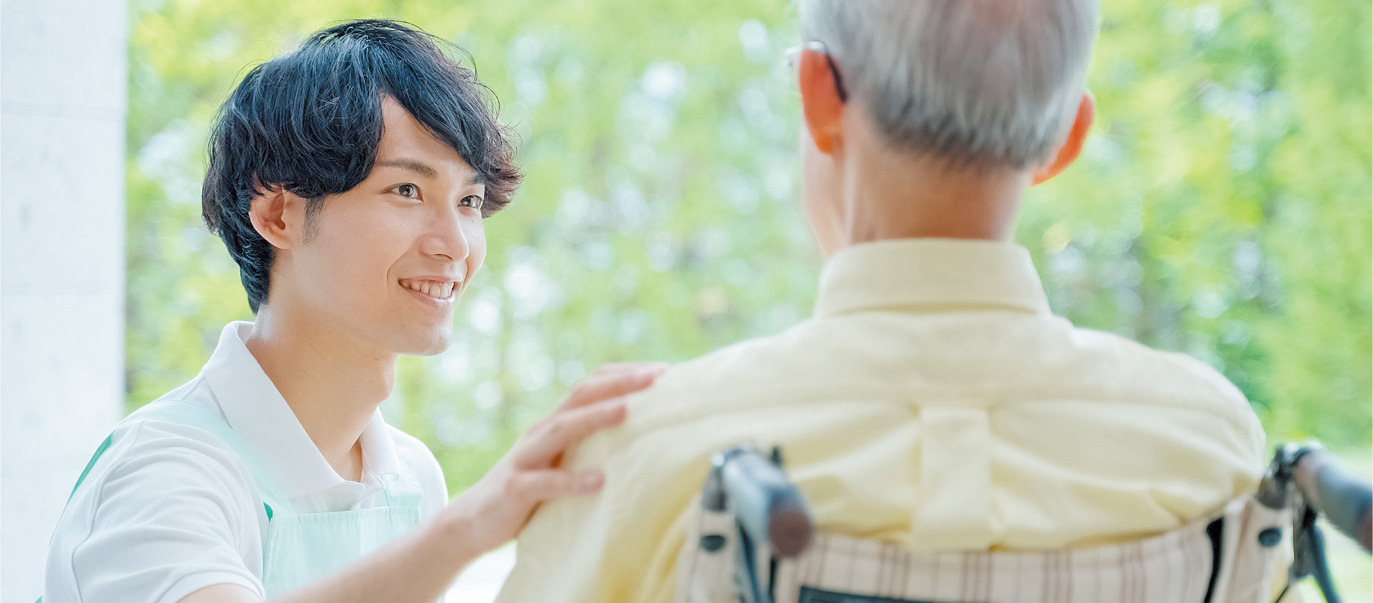 車椅子の男性の肩に手を添える介護士