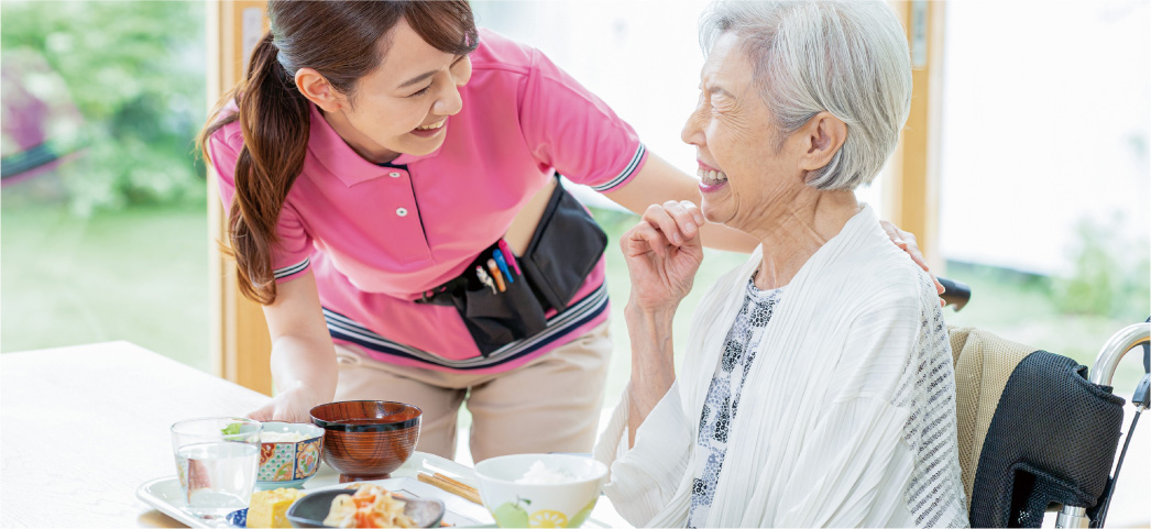 食事をしている女性の肩に手を添える介護士